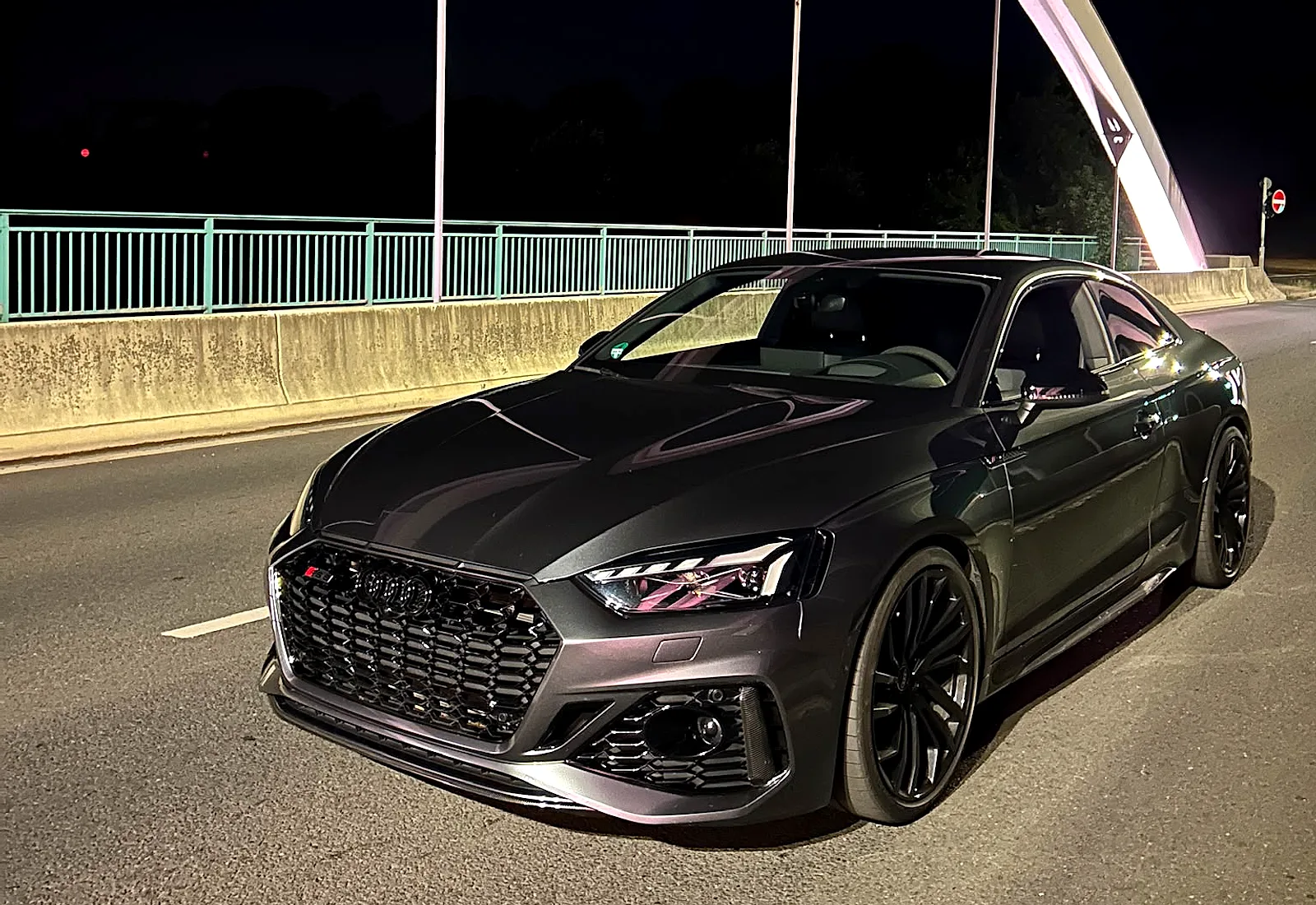 Audi RS 5 Coupé in Grau bei Nacht auf einer Brücke, Frontansicht schräg von links